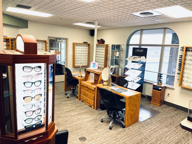 An optical shop with two desks in the center as well as glasses on wall displays and rotating displays